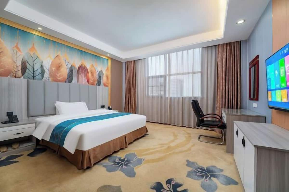 Ein Hotelzimmer mit Bett, Schreibtisch, Stuhl, Fernseher und einem großen Fenster mit Vorhängen.