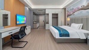 Ein modernes Hotelzimmer mit Bett, Schreibtisch, Stuhl, Fernseher und Küchenzeile.