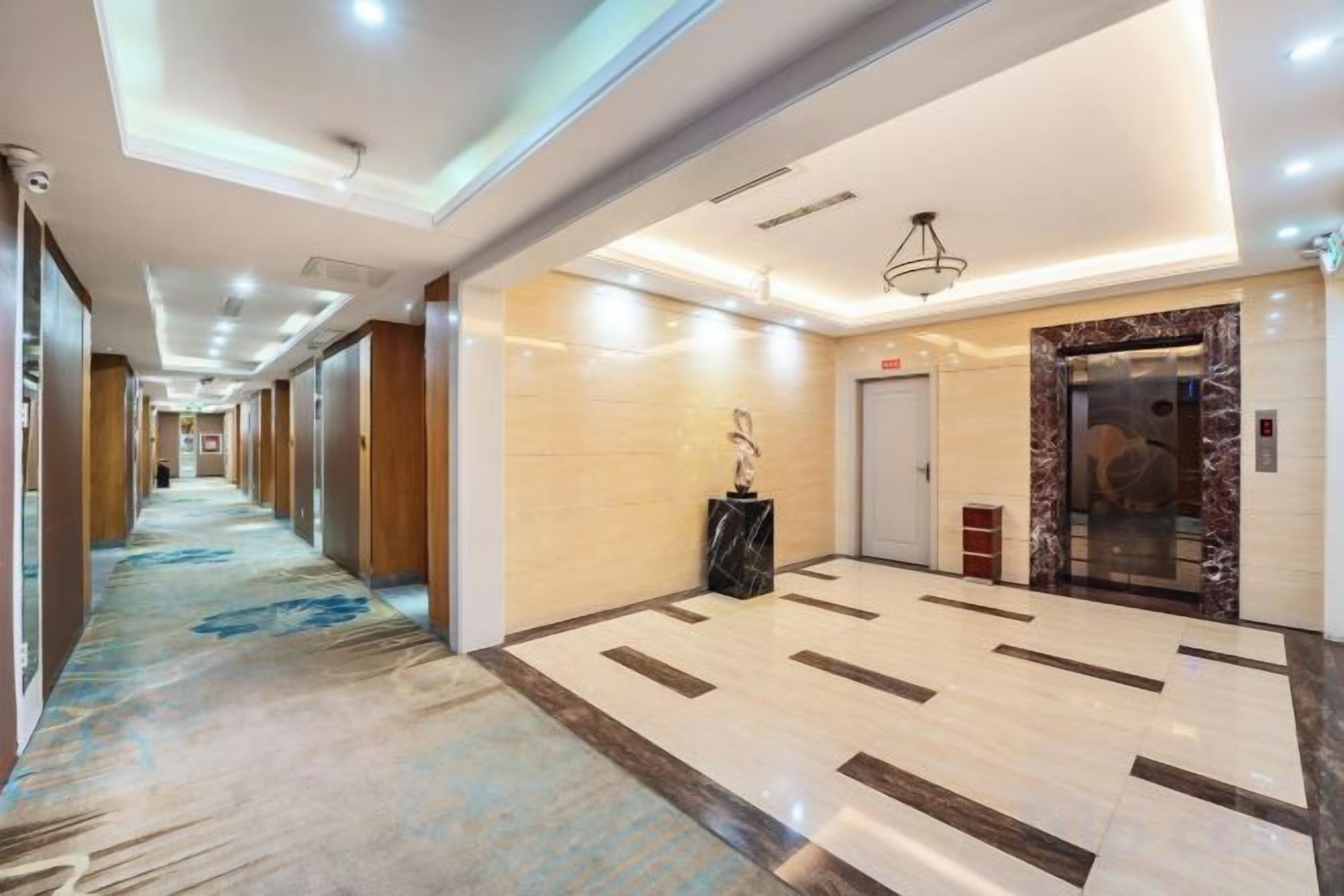 A hotel corridor with a carpeted floor, a marble reception desk, and an elevator.