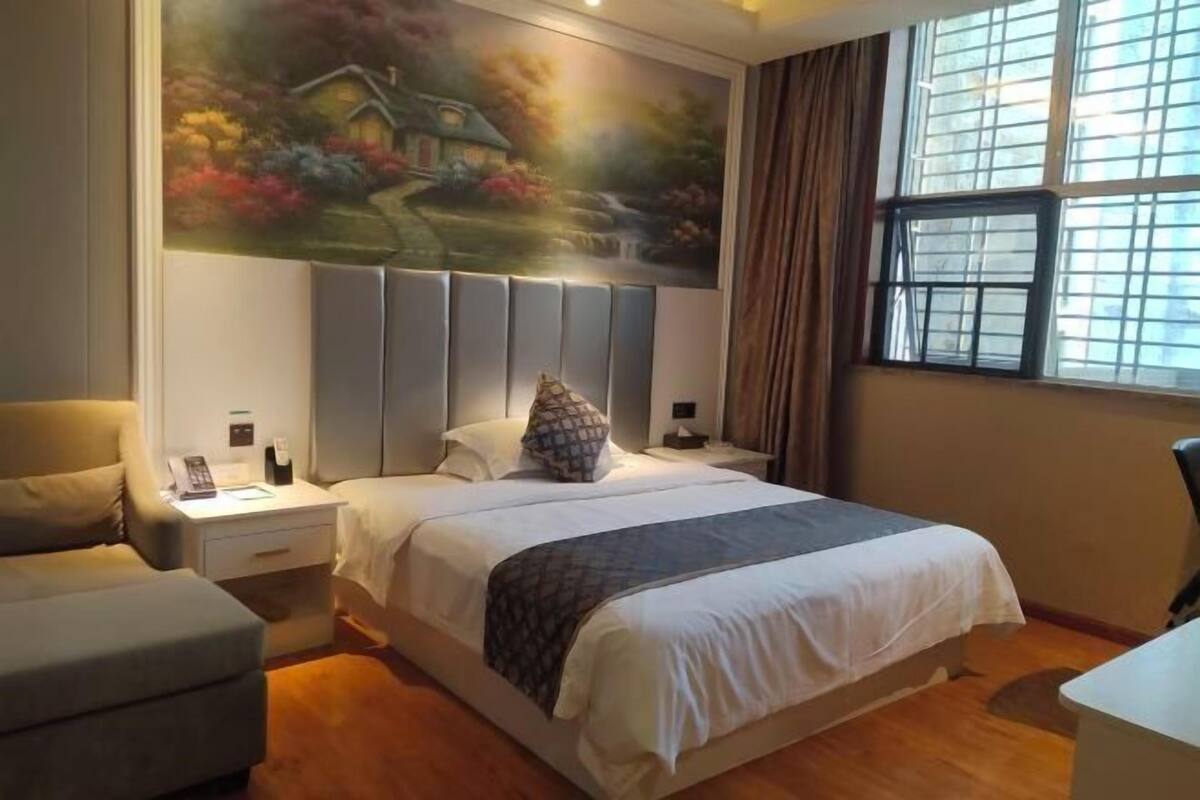 Ein Schlafzimmer mit einem großen Bett, einem Nachttisch, einem Sessel, einem Schreibtisch und einem Fenster mit Vorhängen.