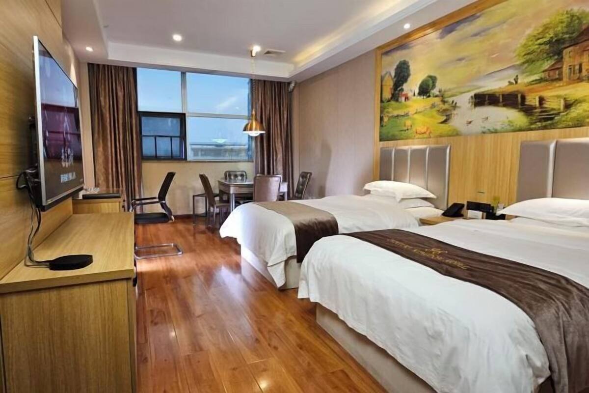 Ein Hotelzimmer mit zwei Betten, einem Schreibtisch mit Fernseher, einem Bild an der Wand und Blick ins Freie.