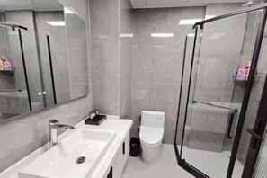 Une salle de bain moderne avec un grand miroir, un lavabo blanc, des toilettes et une douche séparée par une paroi de verre.
