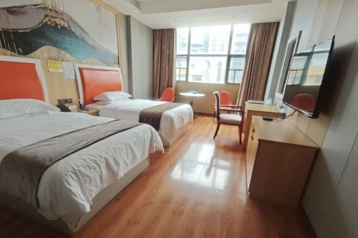 Une chambre d’hôtel avec deux lits, un bureau, une chaise, une télévision et une fenêtre avec des rideaux.