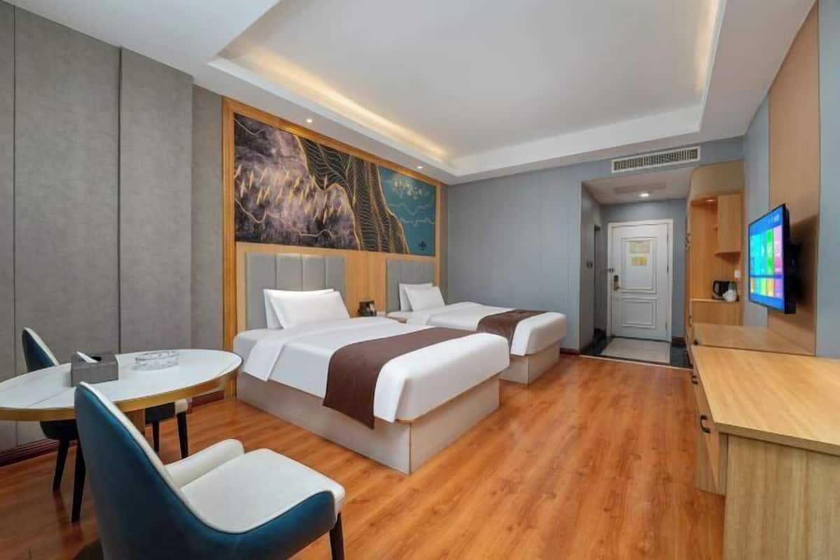 Ein Hotelzimmer mit zwei Betten, einem Schreibtisch, einem Sessel, einem Fernseher und einem Bild an der Wand.
