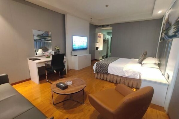 A hotel room with a bed, a desk with a computer, a chair, a small table, and a TV.