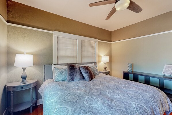 A bedroom with a bed, two bedside tables with lamps, a ceiling fan, and a nightstand with a decorative item.