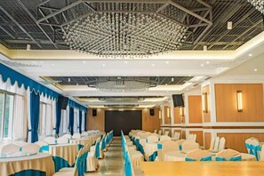 A banquet hall with rows of tables and chairs, a high ceiling with a geometric light fixture, and a stage at the far end. - Jinyu Hotel (Weixi)