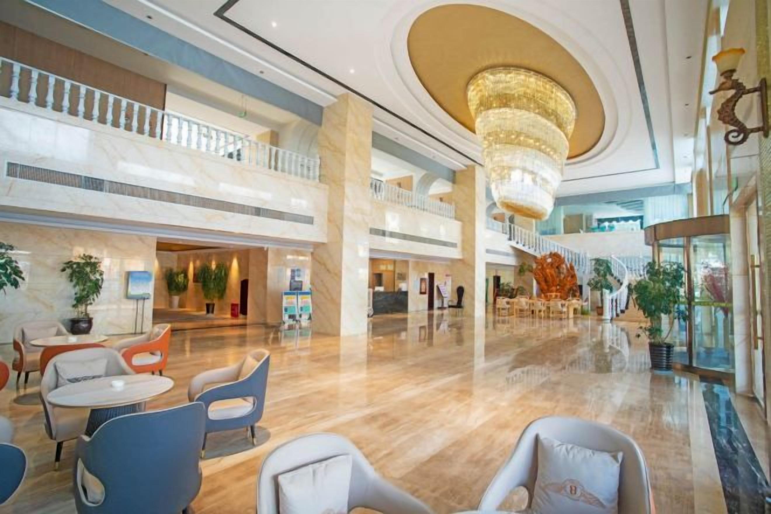 A spacious lobby with a high ceiling, marble flooring, and a grand chandelier.