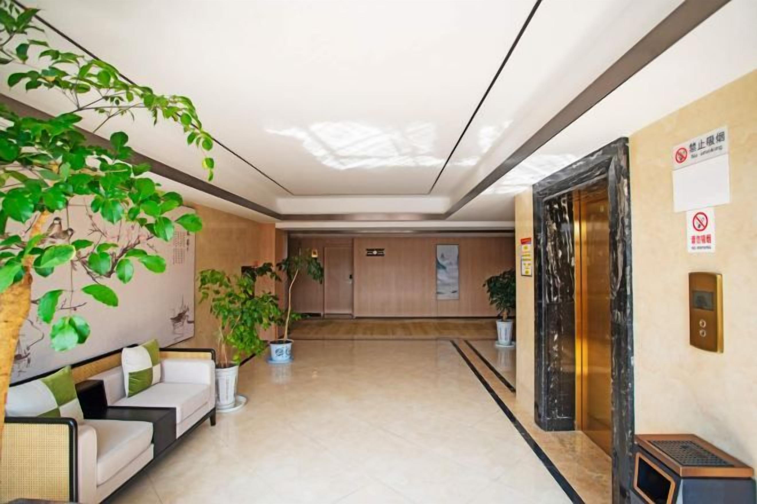 Een hotellobby met een receptiebalie, een zithoek, potplanten en een lift.