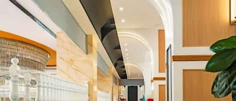 A modern hotel lobby with a marble reception desk, a staircase, and a large plant.
