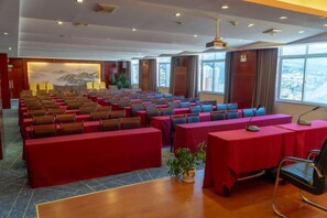 A conference room with rows of tables and chairs, large windows, and a stage area. - Jinyu Hotel (Weixi)