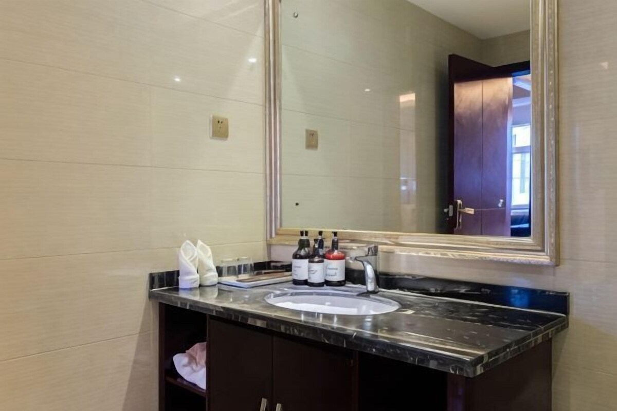 Un baño con un espejo grande, un lavamanos y artículos de aseo en la encimera.