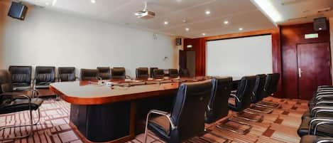 A conference room with a long table, multiple chairs, a projector screen, and a carpeted floor.