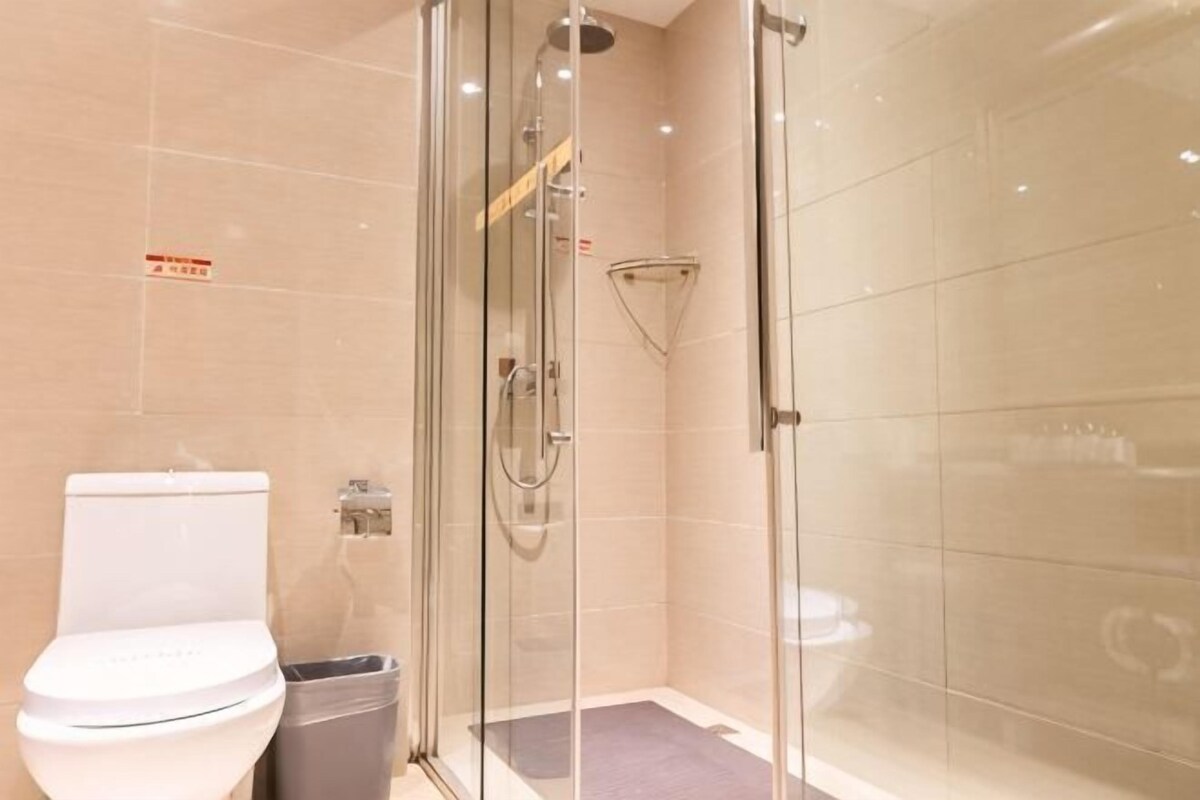 Cabina de ducha con paredes de vidrio, un inodoro y un cesto de basura en un baño moderno.