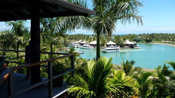 A resort with a pool, palm trees, and boats on a clear day.