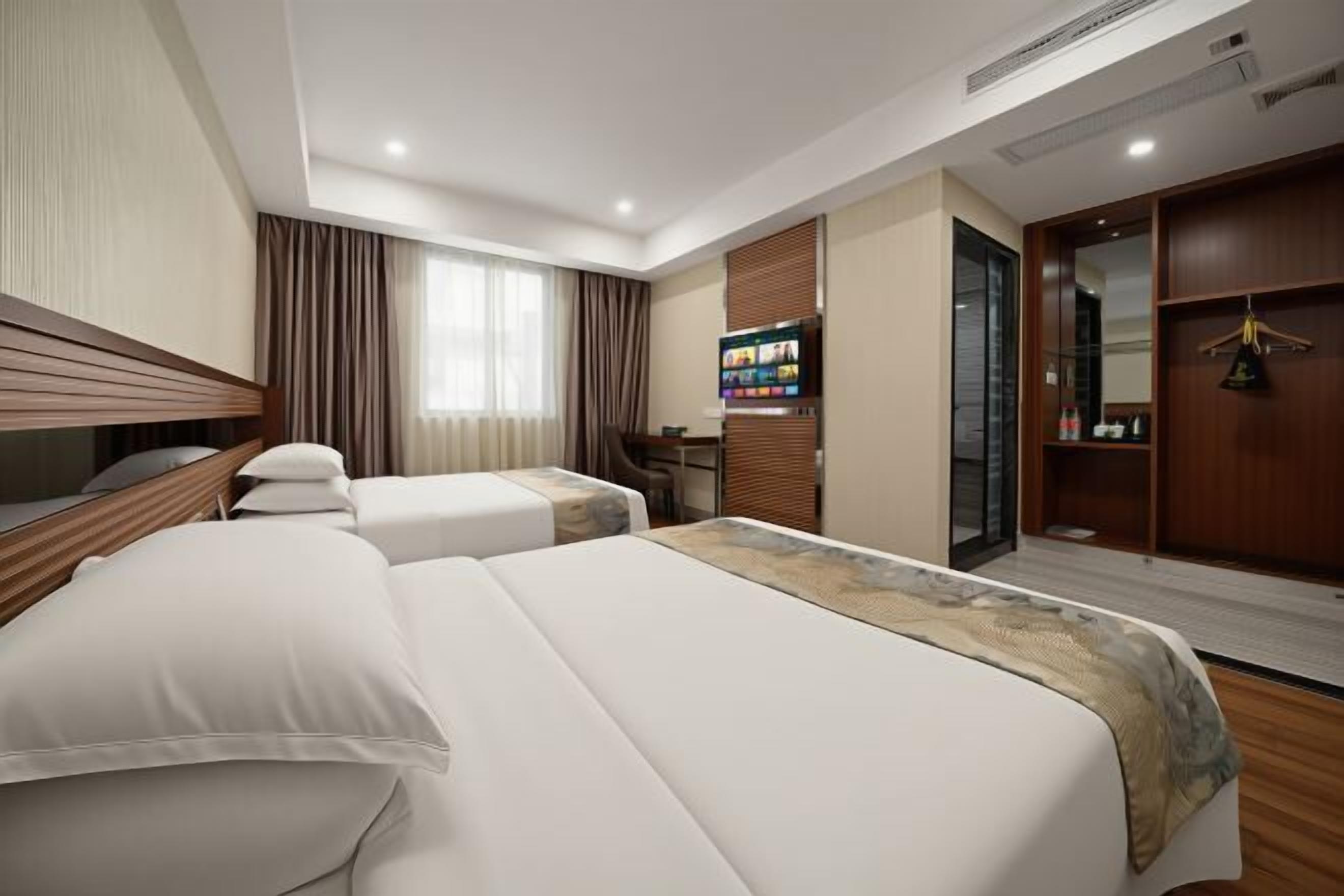 Une chambre d’hôtel avec deux lits, une télévision, un minibar et une salle de bain avec un miroir.