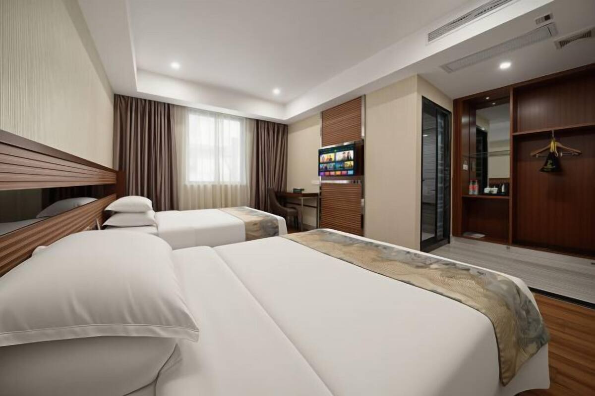 Habitación de hotel con dos camas, televisión, minibar y baño con espejo.