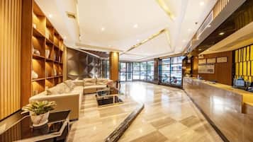 Un moderno vestíbulo de hotel con una recepción, zona de estar y un ventanal que proporciona luz natural.