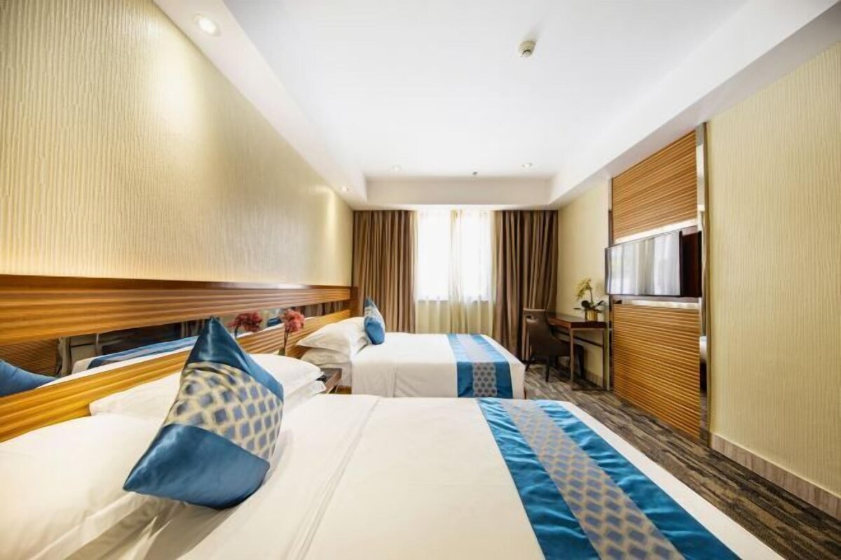A hotel room with two beds, a desk, a chair, and a window with curtains.