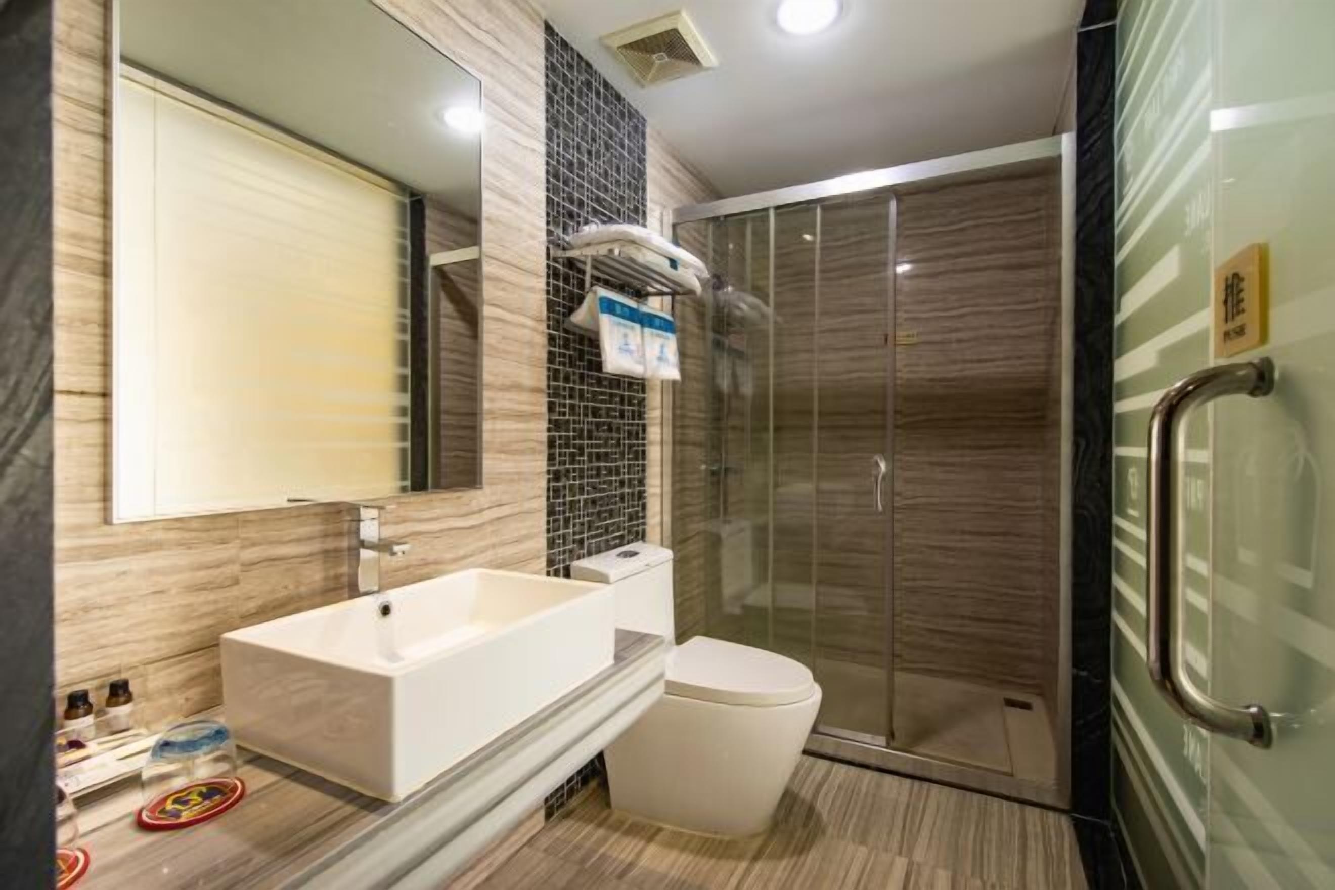 Un baño moderno con un espejo grande, una bañera, un inodoro y ducha con mampara de vidrio.