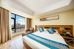 A hotel room with a large bed, a desk, a chair, and a view of the cityscape through large windows. - Park Lane Yiju Hotel (Taishan Commercial City Qiaohu Road) (Taishan)