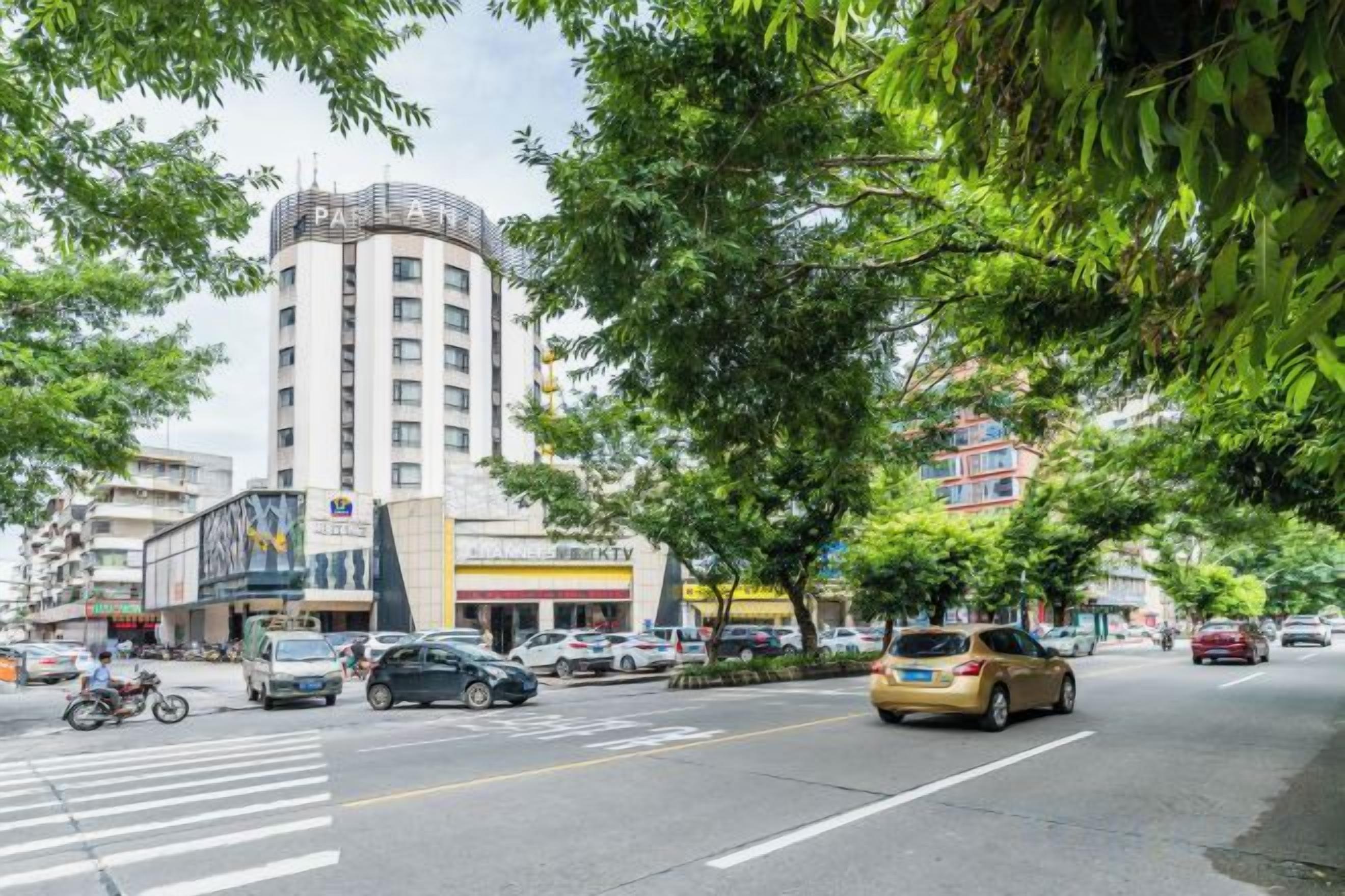 A street view with a hotel, cars, and trees.