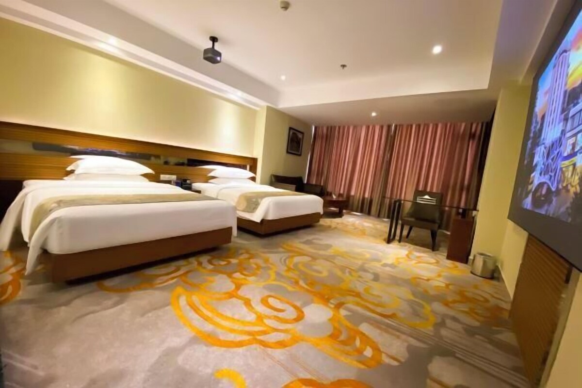 A hotel room with two beds, a large mirror, a television, and a patterned carpet.