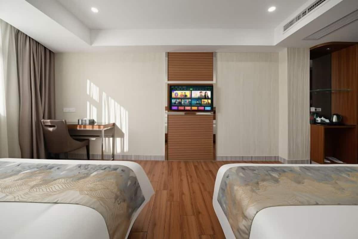 A hotel room with two beds, a desk, a TV, and a wardrobe.