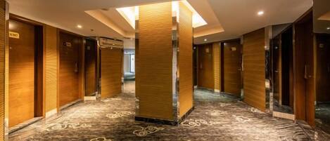 Un pasillo de hotel con puertas de madera, alfombra estampada y un pilar central.