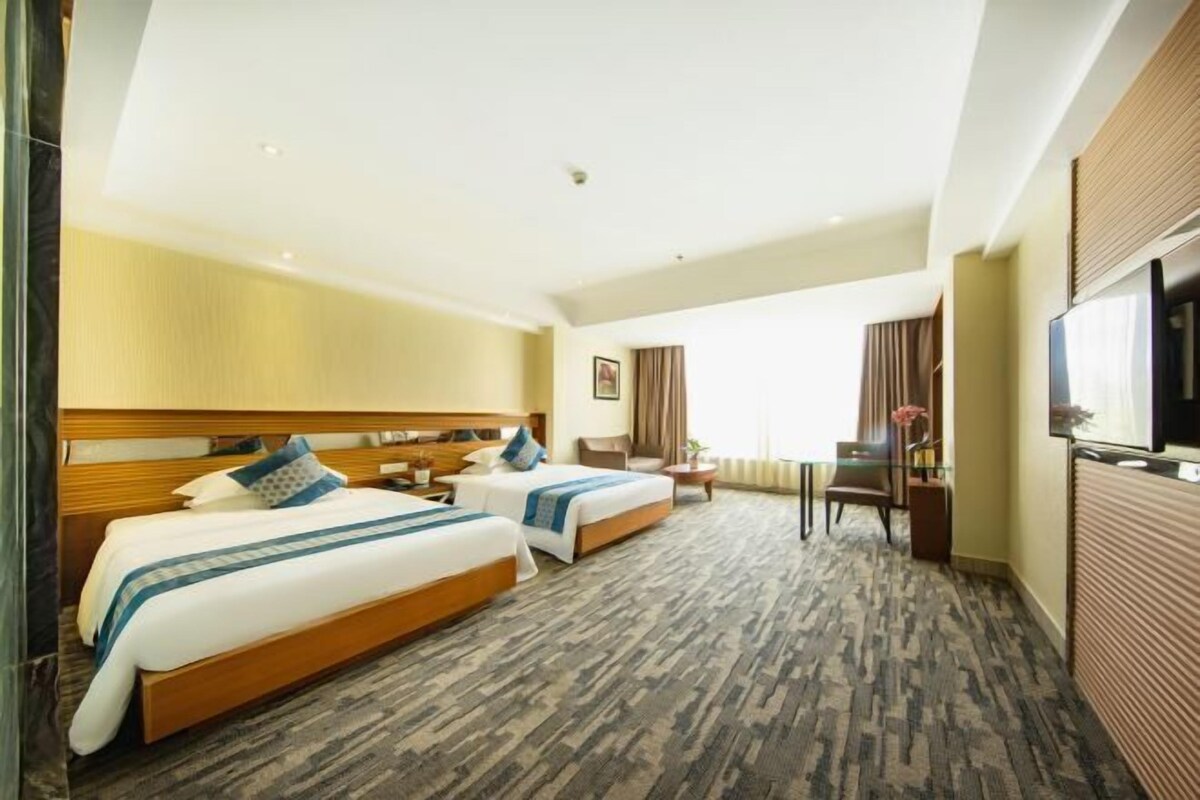 A hotel room with two beds, a desk, a chair, a TV, and a window with curtains.