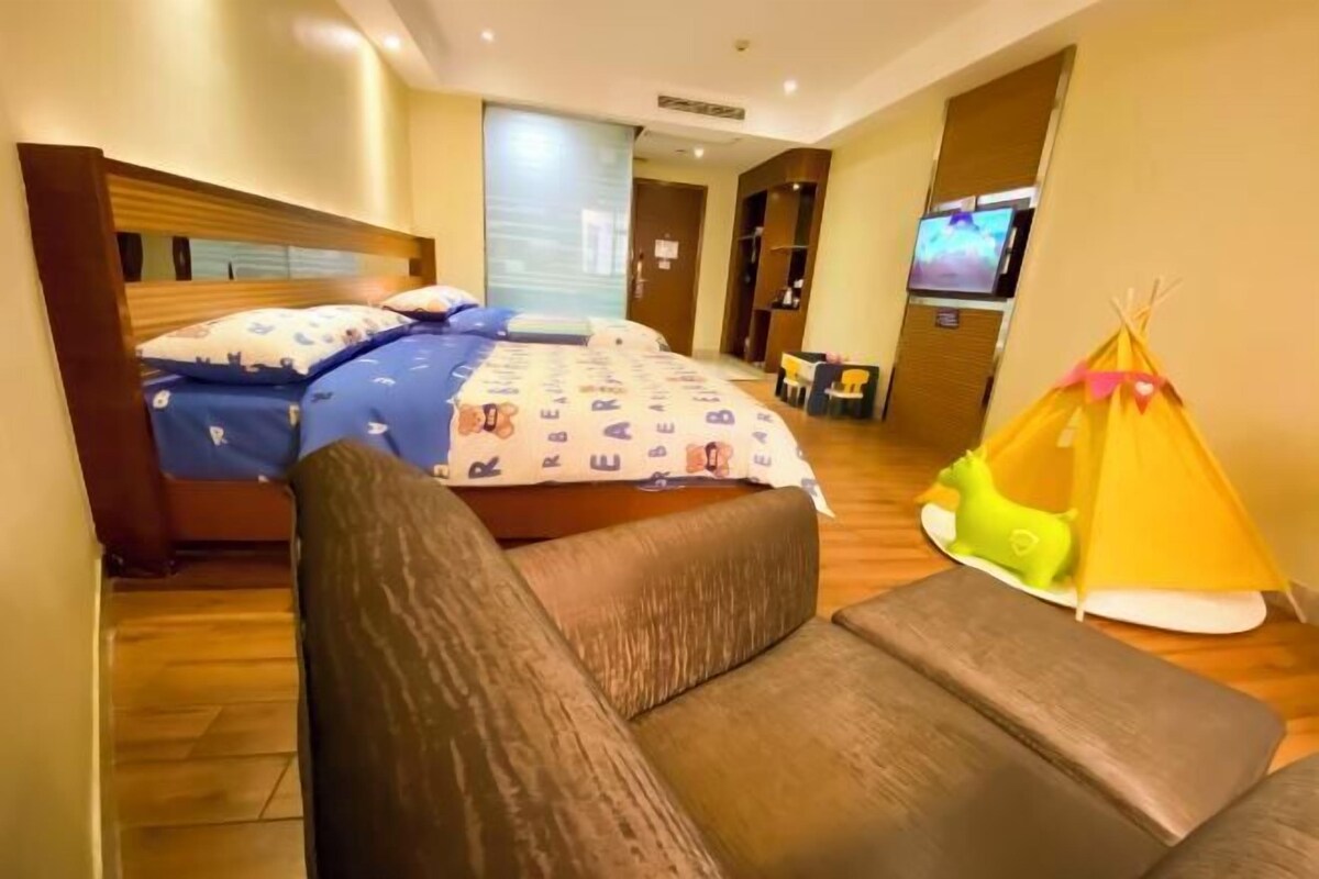 A bedroom with a bed, a sofa, a television, and a yellow tent.