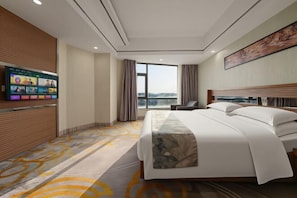 Ein Hotelzimmer mit einem großen Bett, einem Wandfernseher, einem Fenster mit Vorhängen und Blick auf die Stadt.