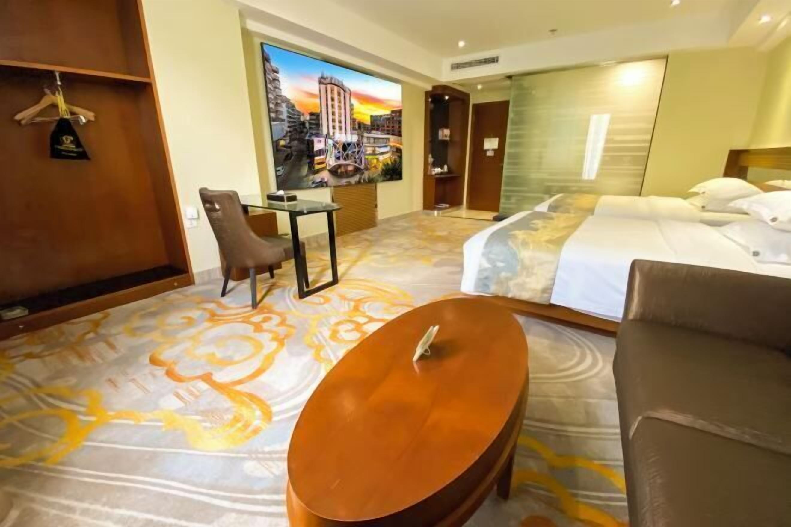 Hotelkamer met een bed, een bureau, een stoel en een groot raam met uitzicht op de stad.