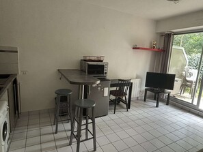 Une cuisine compacte Ă©quipĂ©e dâun four Ă micro-ondes, dâun petit coin repas avec des tabourets, dâune tĂ©lĂ©vision et dâune fenĂȘtre donnant sur un espace verdoyant.