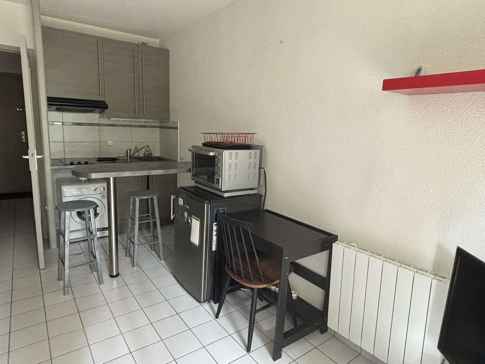 Cocina compacta con microondas, lavaplatos y un pequeño comedor con una silla.