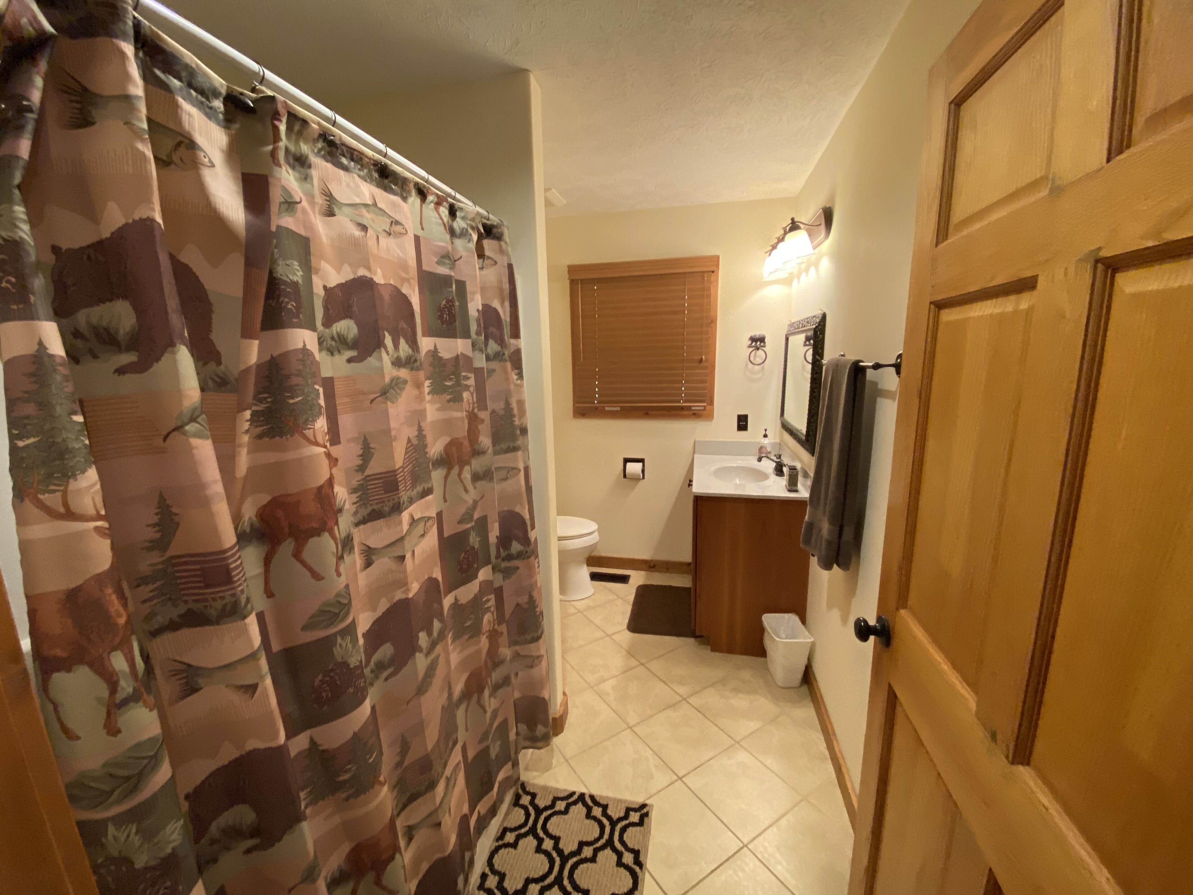 Un baño con cortina de ducha estampada con motivos de fauna, un inodoro, un lavamanos y un espejo.