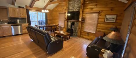 A log cabin interior with a dining area, seating, a fireplace, and a kitchen.