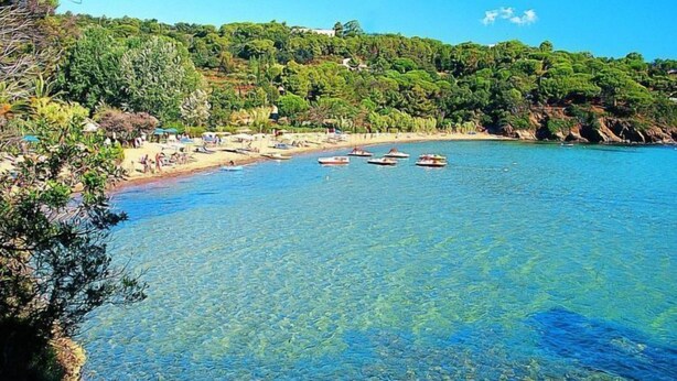 A coastal beach with clear water, boats, and a rocky shoreline.