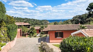 A coastal property with terracotta-roofed buildings, a paved driveway, and lush greenery.