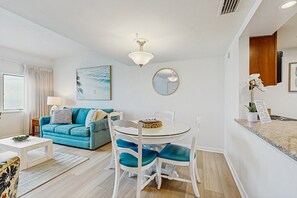 Relax in this inviting living room with a round dining table, blue sofa, and a beautiful coastal painting.