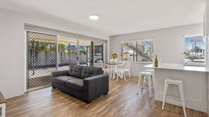 A modern living room with a grey sofa, white chairs, and a kitchen area with a white countertop and bar stools. - Sea-Hi Beachside Apartment (Maroochydore)
