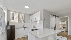A modern kitchen with white cabinetry, a central island, and a built-in dishwasher. - Sea-Hi Beachside Apartment (Maroochydore)