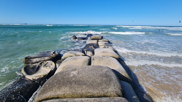 A stone breakwater leading to a beach with waves crashing against it. - Sea-Hi Beachside Apartment (Maroochydore)