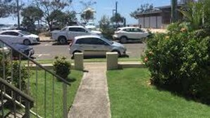 A parking lot with several cars, a grassy area, and a building in the background. - Sea-Hi Beachside Apartment (Maroochydore)