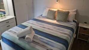 A neatly made bed with striped bedding, a bedside table with a plant, and a wall-mounted light fixture. - Sea-Hi Beachside Apartment (Maroochydore)