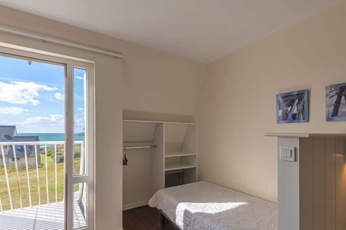 A bedroom with a bed, a closet, and a balcony with a view of the sea.