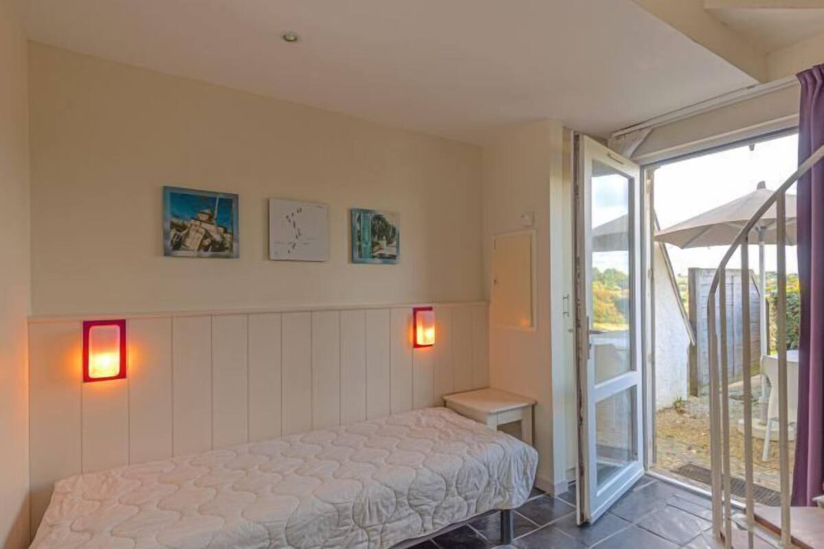 A bedroom with a bed, a small table, and a sliding glass door leading to an outdoor area.