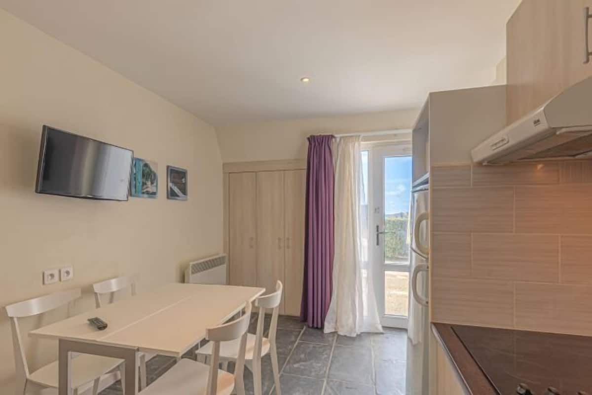 A modern kitchen with a dining area, a TV mounted on the wall, and a sliding glass door leading to an outdoor area.
