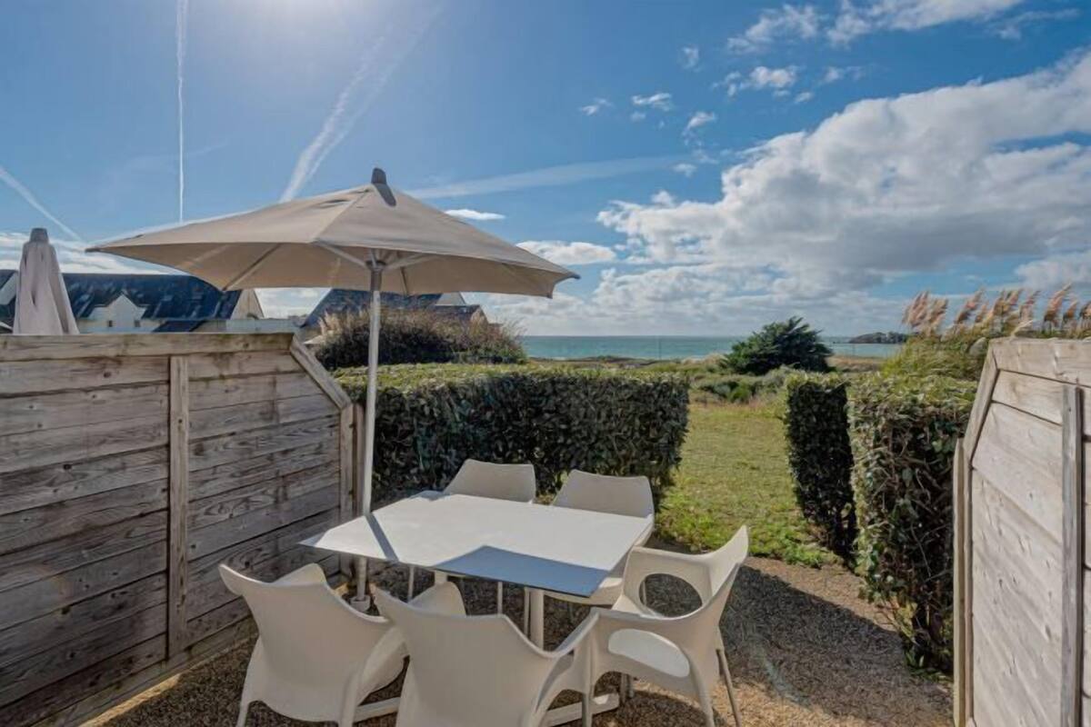 An outdoor patio with a table and chairs, a large umbrella, and a view of the sea.