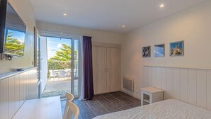 Habitación de hotel con cama, escritorio, silla, televisor y puerta corredera a un balcón.